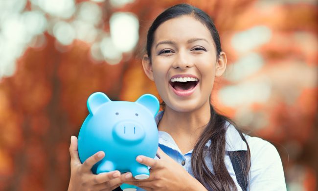 Closeup portrait happy, smiling business woman, bank employee holding piggy bank, isolated outdoors indian autumn background. Financial savings, banking concept. Positive emotions, face expressions
